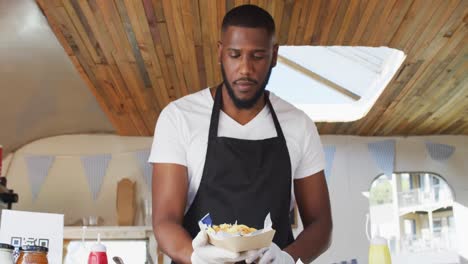 Portrait-of-african-american-man-wearing-apron-smiling-while-serving-food-in-food-truck