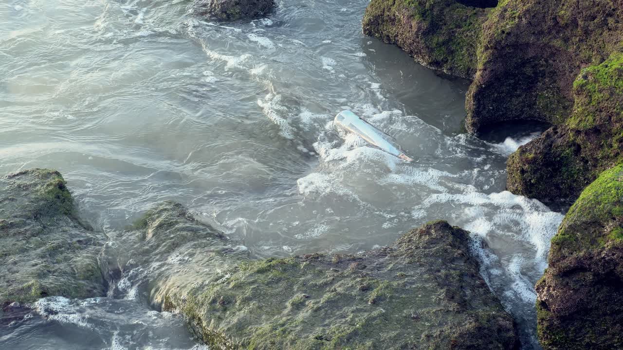 Static view of a bottle stuck between the rocks into the sea. Daylight
