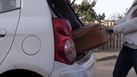 mujer sacando una vieja maleta marrón del maletero del coche.