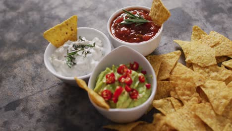 Close-up-of-nachos-and-variety-of-sauces-on-black-surface