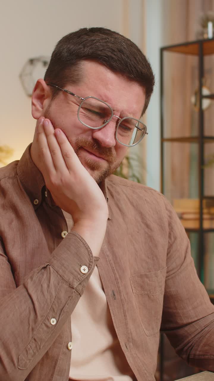 Caucasian young man freelancer sitting at home office table feeling toothache touching mouth at home