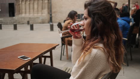 una joven sentada en un café bebiendo un vaso de vino tinto