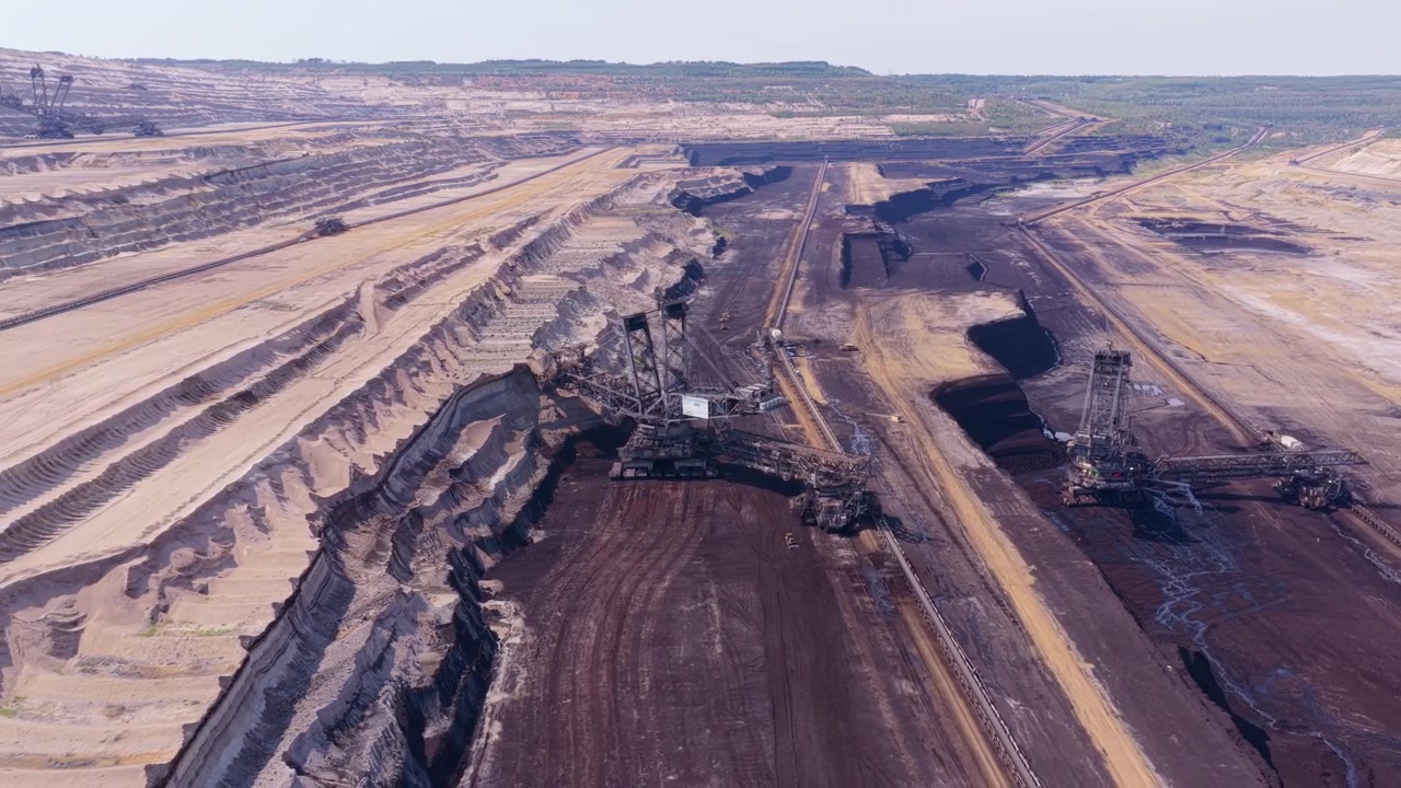 Massive bucket wheel excavator machines operating in a vast open pit coal mine. Aerial view of the heavy equipment digging into the earth