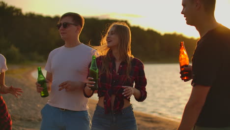 jóvenes adolescentes están bailando en la fiesta al aire libre con cerveza. están disfrutando de la puesta de sol de verano con amigos en la playa en la hermosa puesta de sol roja.