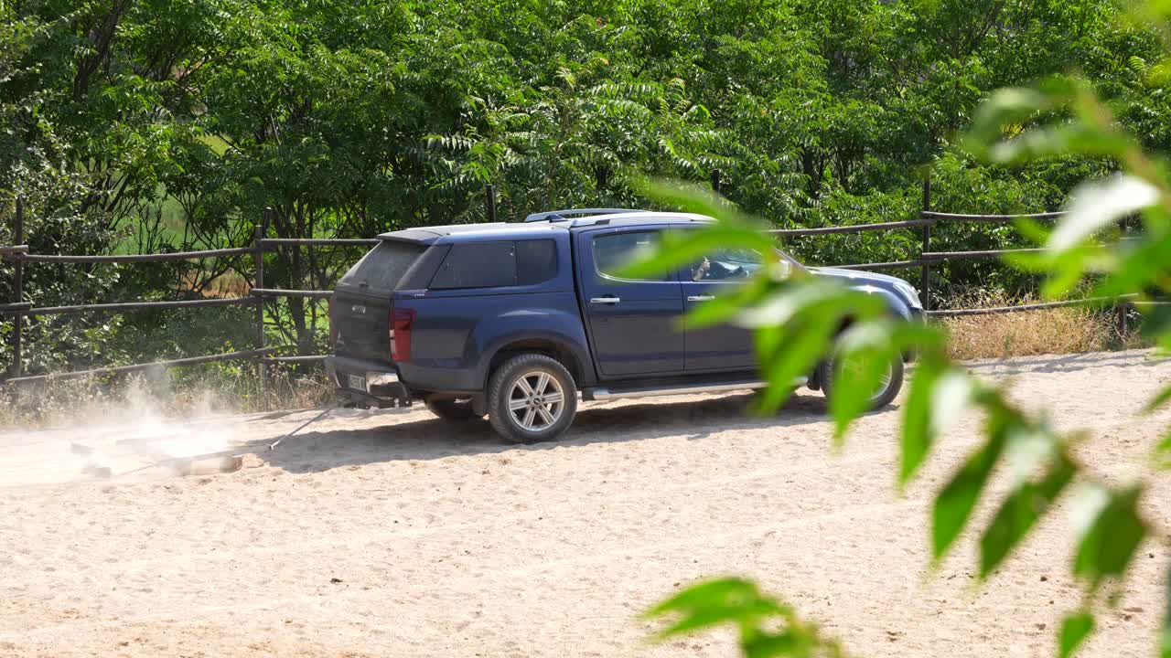 Utility car with a drag raises dust while smoothing a track among lush vegetation