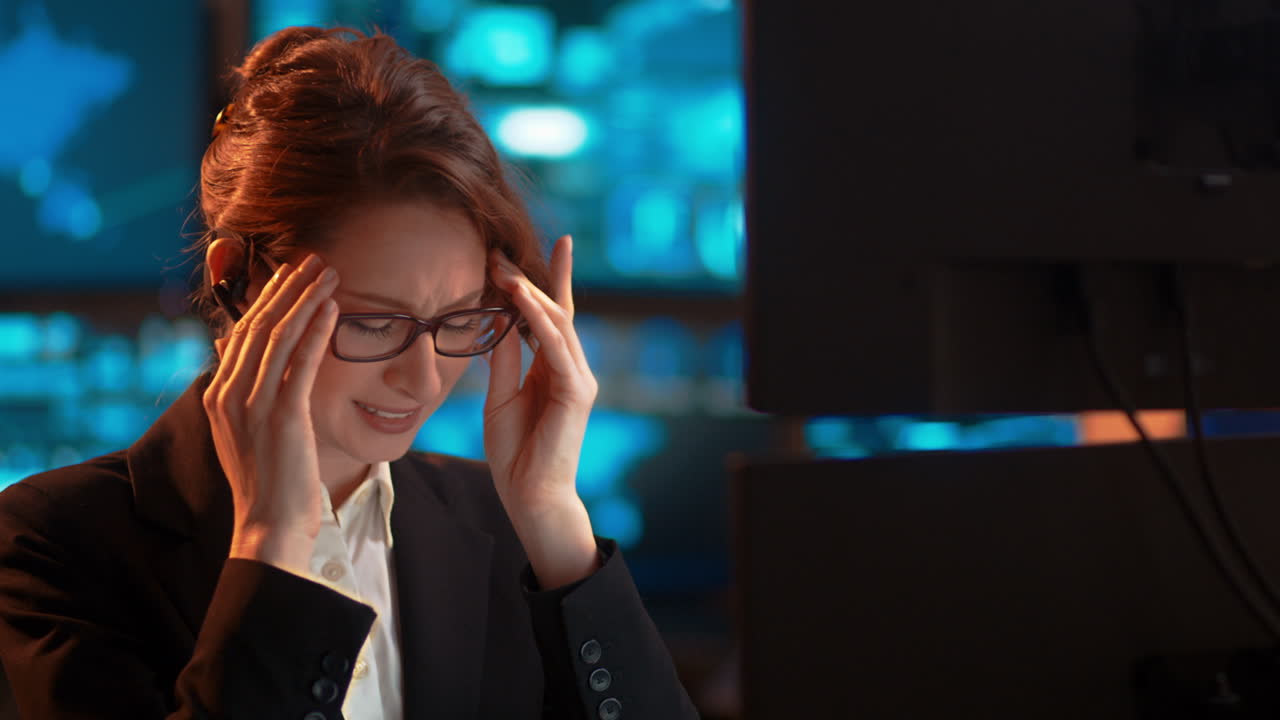 Slow pan, a businesswoman at work talking through her bluetooth headset, in a customer service-type industry, experiencing a major migraine, headache