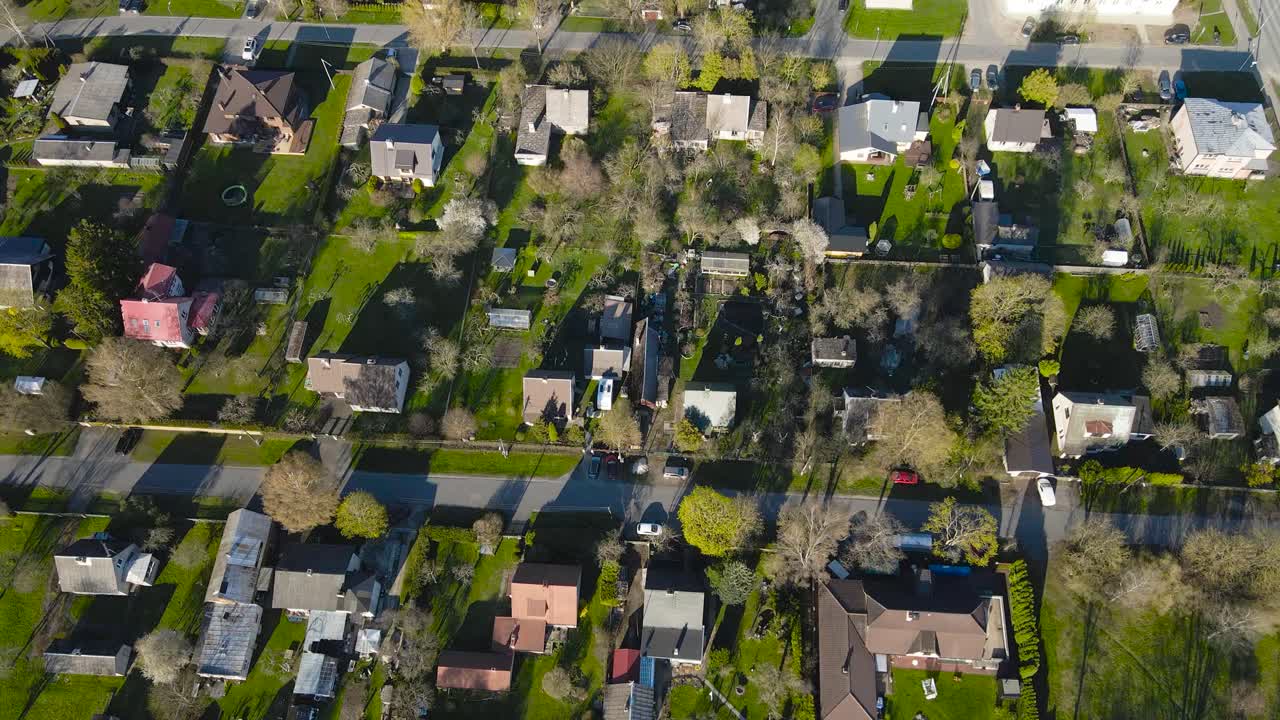 Aerial tilt up shot showing townscape of Saku during springtime, showcasing a residential area with private houses, gardens and lush greenery. View expands to reveal rural charm with urban development