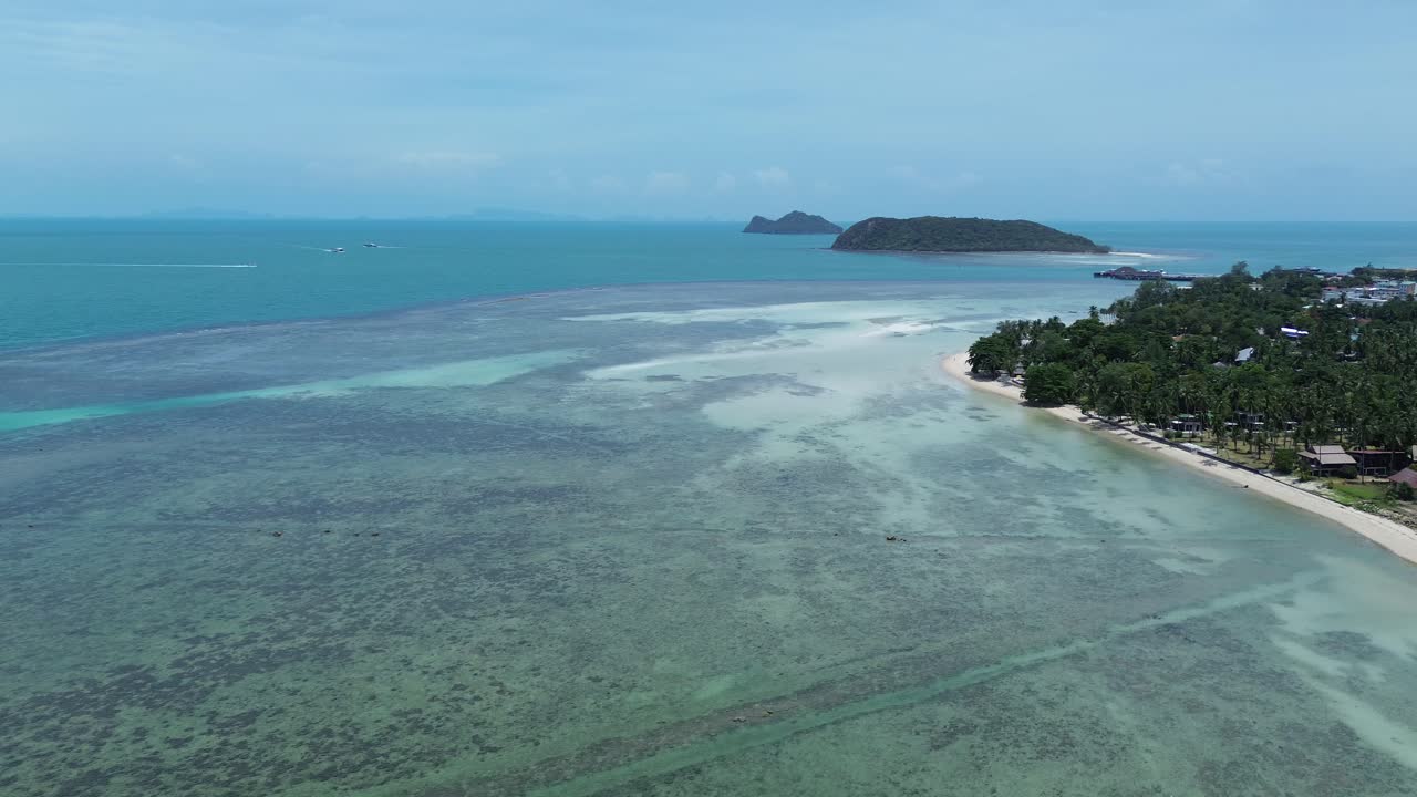 Aerial footage of Thong Sala Beach with a wide sandy shoreline, turquoise sea and lush tropical scenery on Koh Phangan island, Thailand