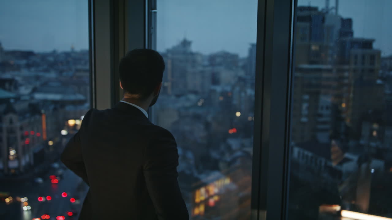 gerente pensativo mirando noche vista de la ciudad en la ventana de la oficina de cerca. trabajador serio