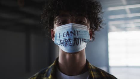 Portrait-of-mixed-race-man-wearing-protest-face-mask-in-empty-parking-garage