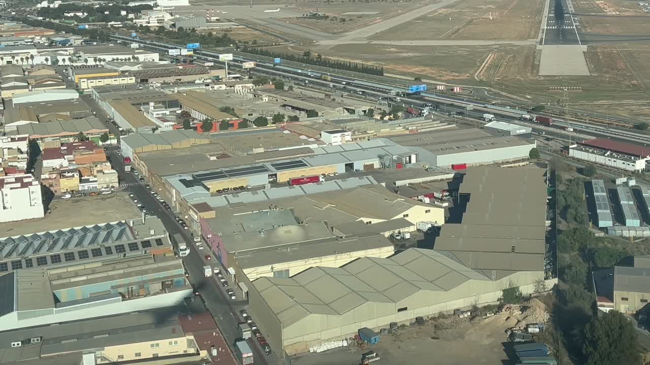 sombra de un avión a reacción como se ve por la cabina de mando sobre los edificios de un parque industrial con la pista de aterrizaje delante