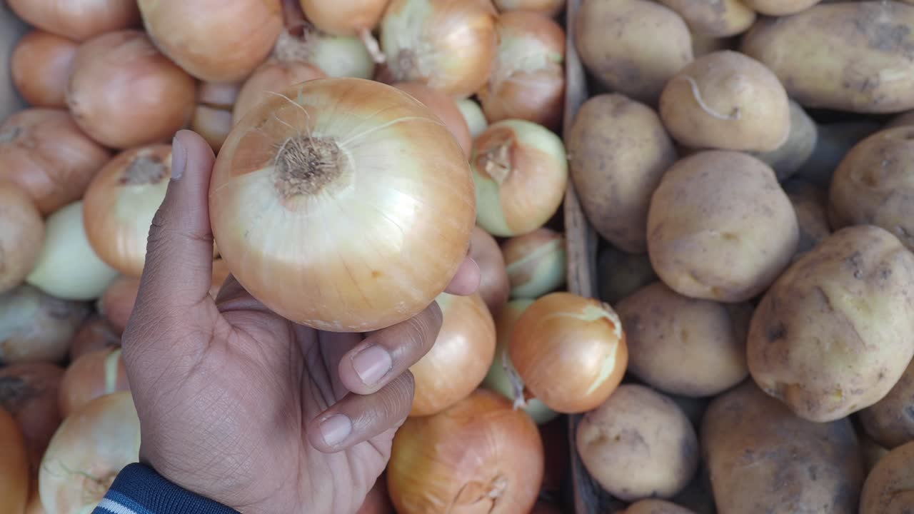 Hand holding an onion with other onions and potatoes in the background