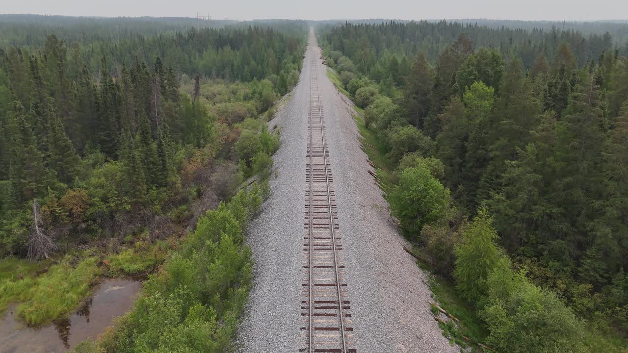 Drone aerial moving backward along train tracks through boreal forest near Gillam Manitoba. Remote northern railway corridor with tracking motion over wilderness landscape