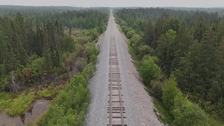 Drone aereo in movimento all'indietro lungo i binari del treno attraverso la foresta boreale vicino a Gillam, Manitoba. Remoto corridoio ferroviario settentrionale con movimento di tracciamento su paesaggio selvaggio.
