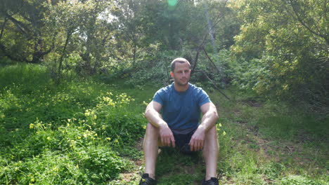 A-handsome-man-sitting-in-a-green-grassy-forest-meadow-on-a-bright-sunny-day-while-thinking-and-pondering-while-enjoying-nature-SLOW-MOTION