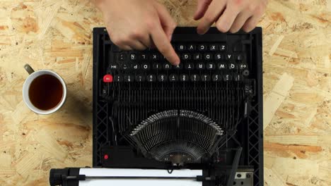 Hands typing on an old vintage typewriter on a wooden desk with a cup of tea