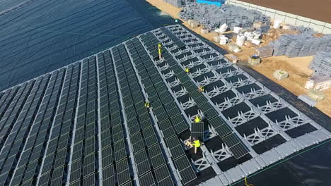 slow aerial pullback over a solar array, showing workers in yellow manipulating components. drone.