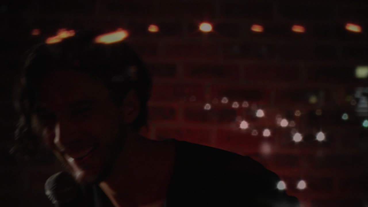 Uomo che solleva il microfono e canta su un piccolo palco musicale, sovrapposizione bokeh sul volto, pubblico coinvolto