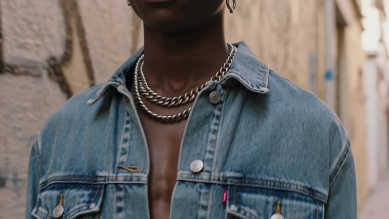 Gående mandlig model modellerer gennem en gyde, kameraet zoomer ind og viser denimjakke, kæder, ringe og graffiti.