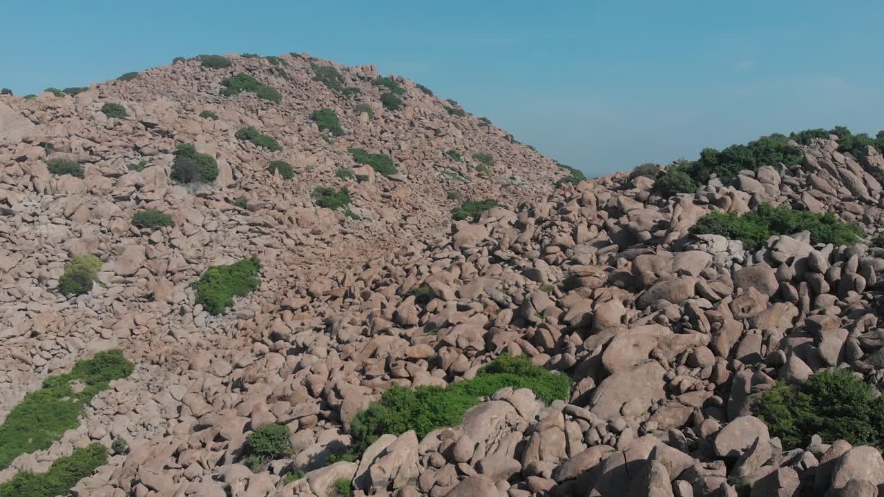 volando a baja altura sobre las rocas que cubren una colina intercalada con arbustos verdes en una zona rural de la india