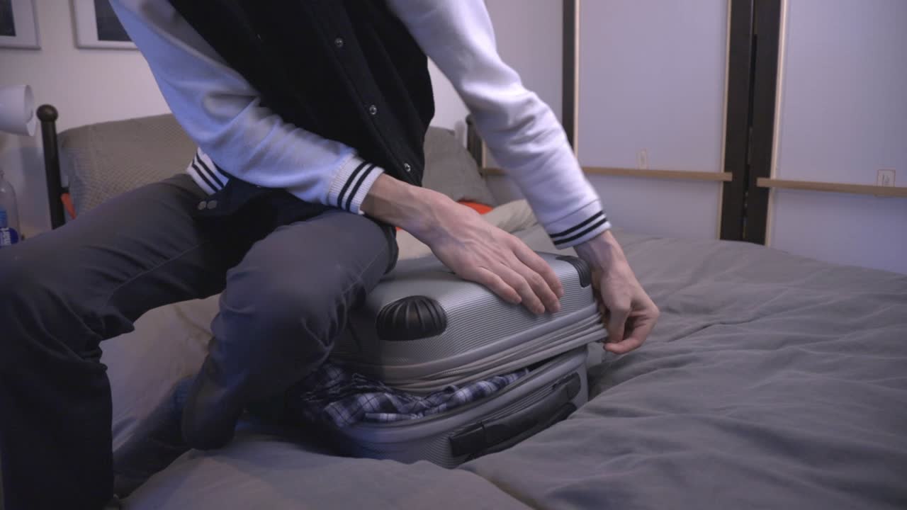 한 청년이 양손으로 닫으려는 과부하 여행 가방에 앉아 있다 - 반신발