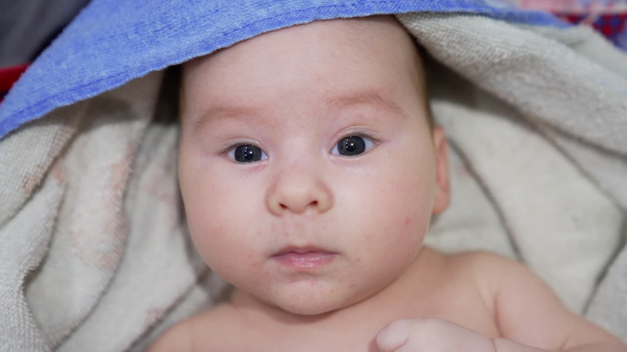 Beautiful kid looking in front of him, lying calmly and peacefully. Baby boy covered in bath towel after washing time. Close up.