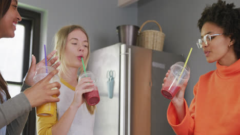 happy diverse teenager girls friends drinking healthy drink in kitchen, slow motion