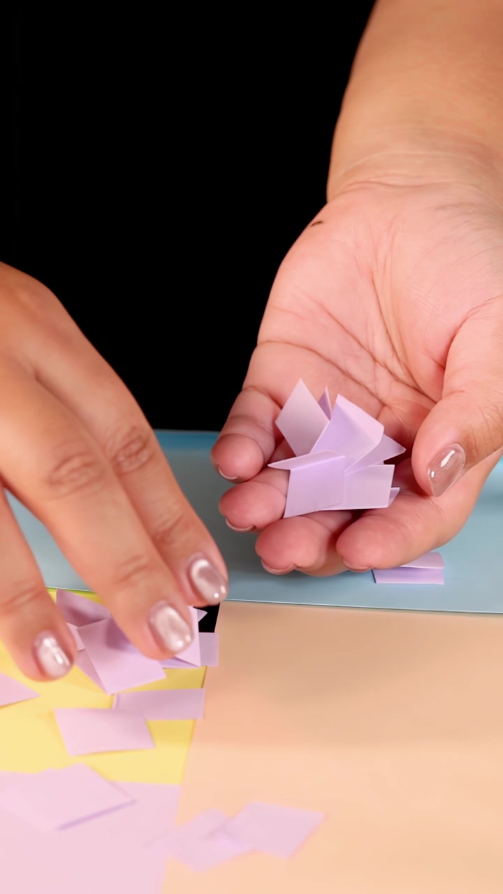 Una mano seleziona e solleva quadrati di carta pastello dal tavolo sotto un'illuminazione da studio brillante e uniforme