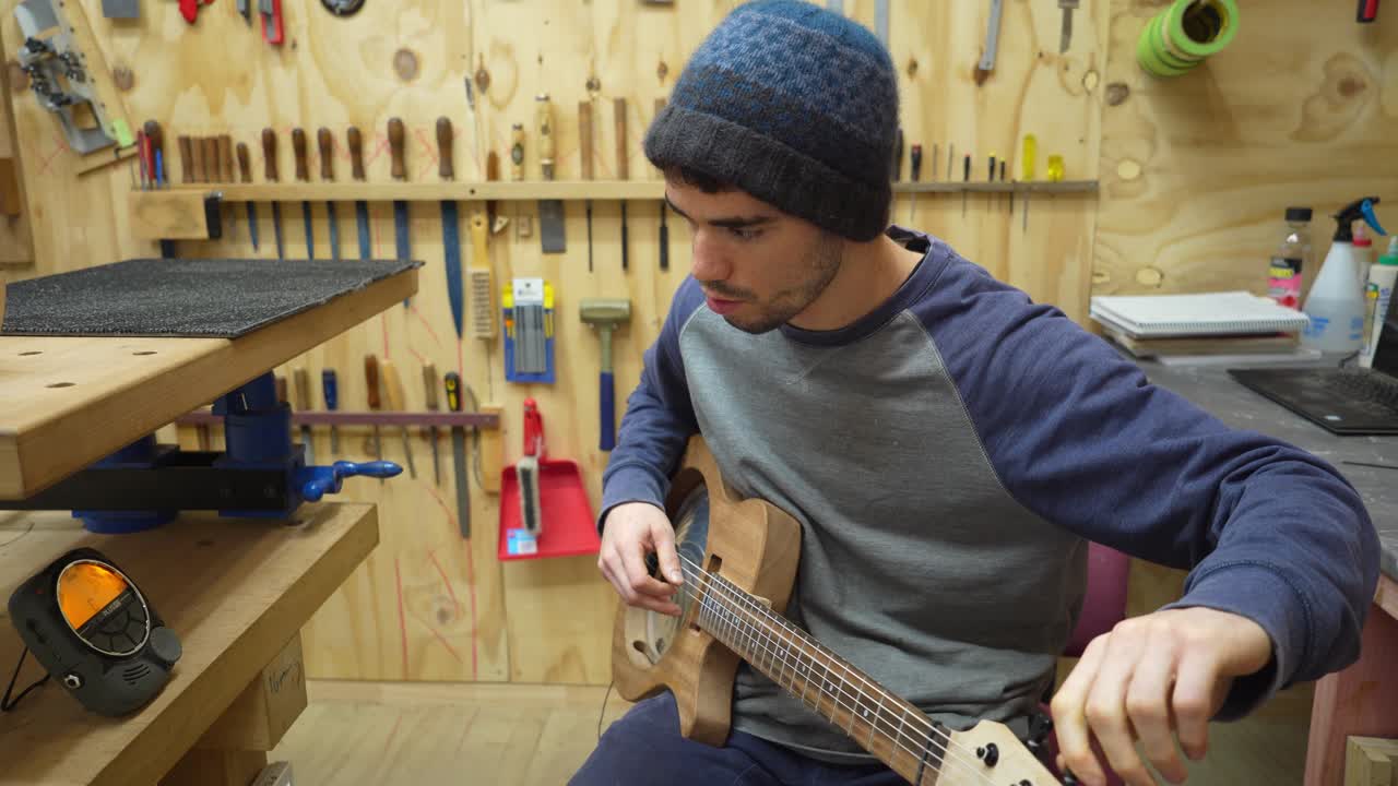 Luthier en taller afina una guitarra de resonador eléctrica personalizada recién construida con afinador digital.
