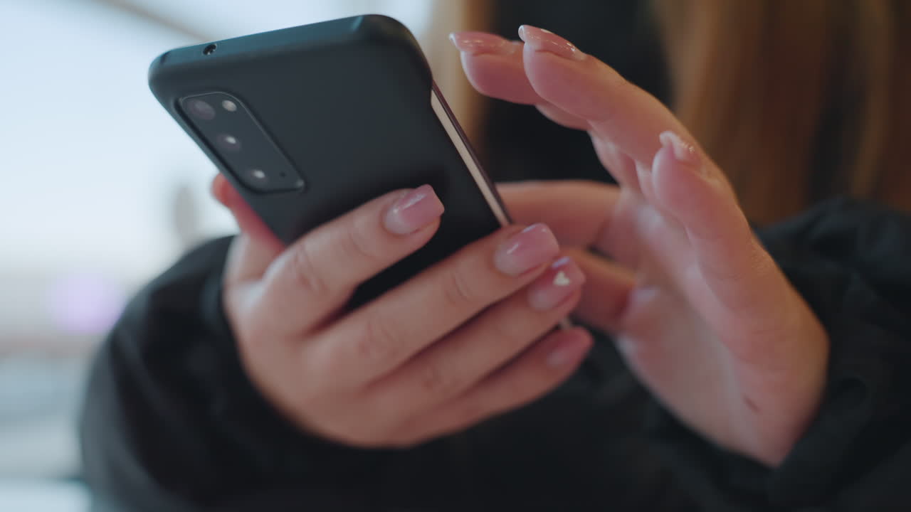 Primo piano di mani che tengono un telefono, donna che controlla messaggi e scorre, unghie curate e custodia protettiva, sfondo bokeh morbido con luce naturale dalla finestra, focus sull'interazione con lo schermo e tocchi delicati.