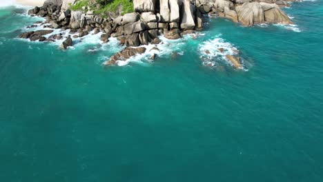 bird eye drone shot of north east point beach, huge rock boulders waves crushing on and turquoise water, mahe seychelles 30fps 1