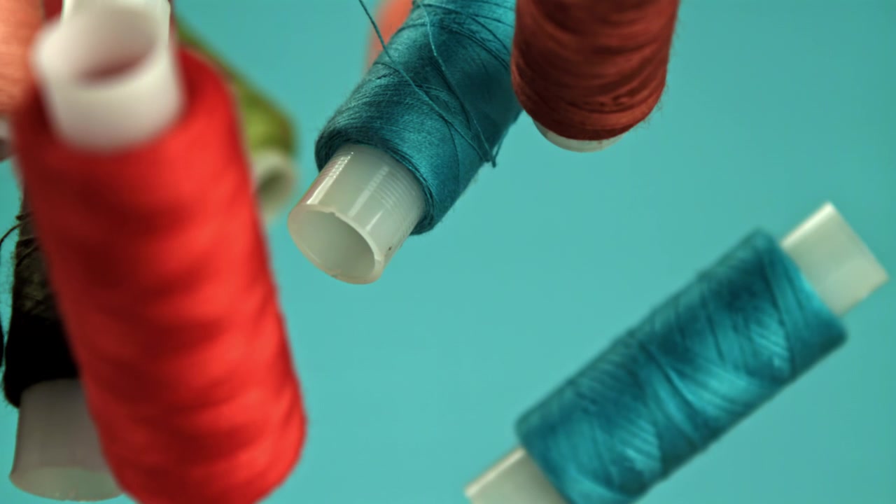 Colorful Spools of Thread Falling in Slow Motion Against a Teal Background