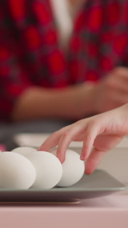 little child hand reaches to eggs while elder sister prepares ebru decor in living room closeup slow motion. unusual easter holiday decoration