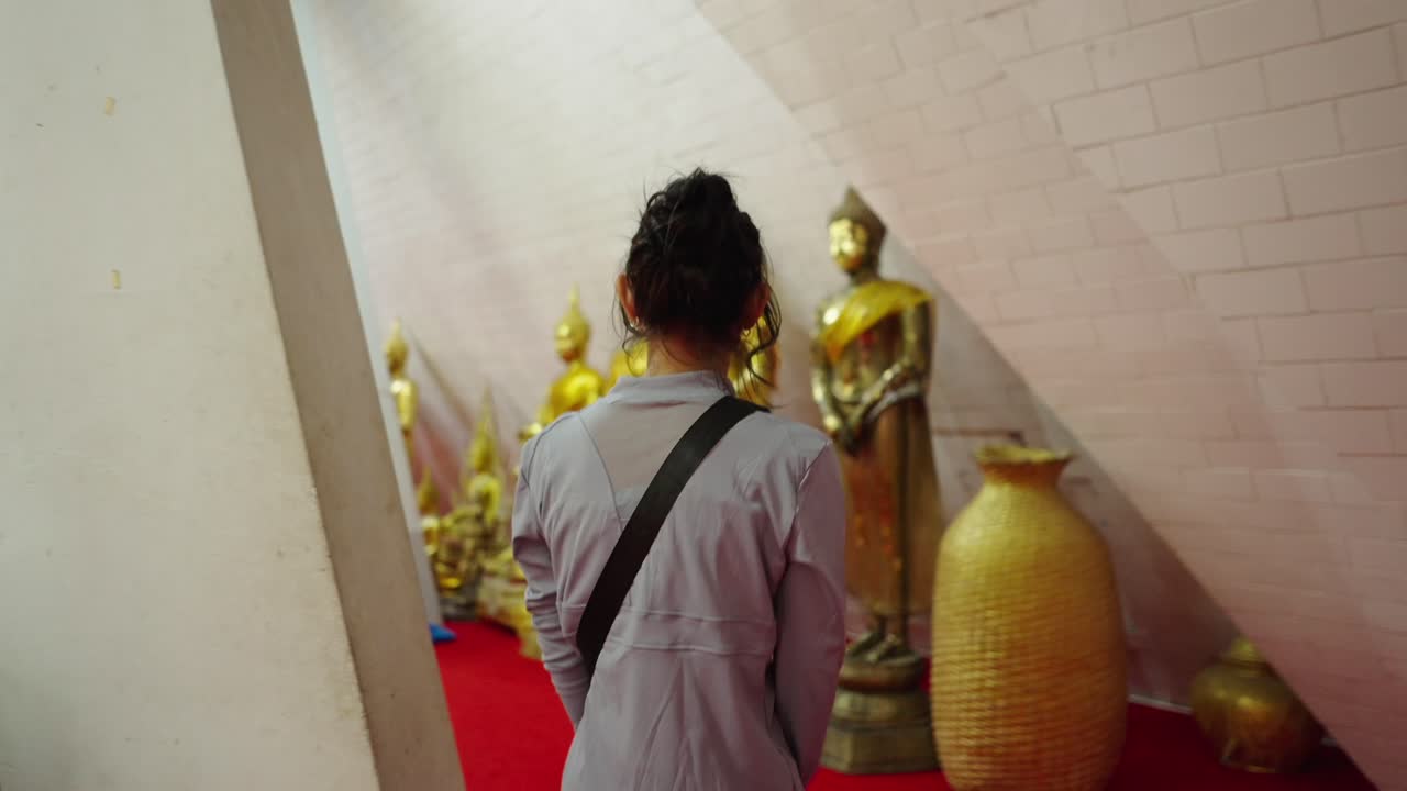 Woman walking past golden Buddha statues in a Buddhist temple
