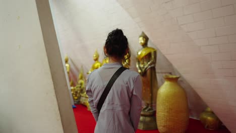 woman walking past golden buddha statues in a buddhist temple