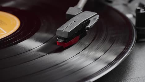 perspective close-up view of record needle with black vinyl spinning on a vintage record player
