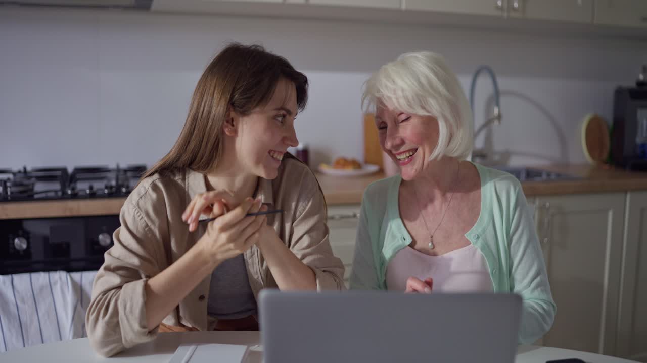 Senior Woman and Young Woman Using Laptop in Kitchen
