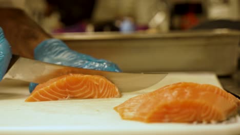 cámara lenta de una gran pieza de salmón siendo cortada por un chef en un restaurante y luego colocada junto a otras rebanadas