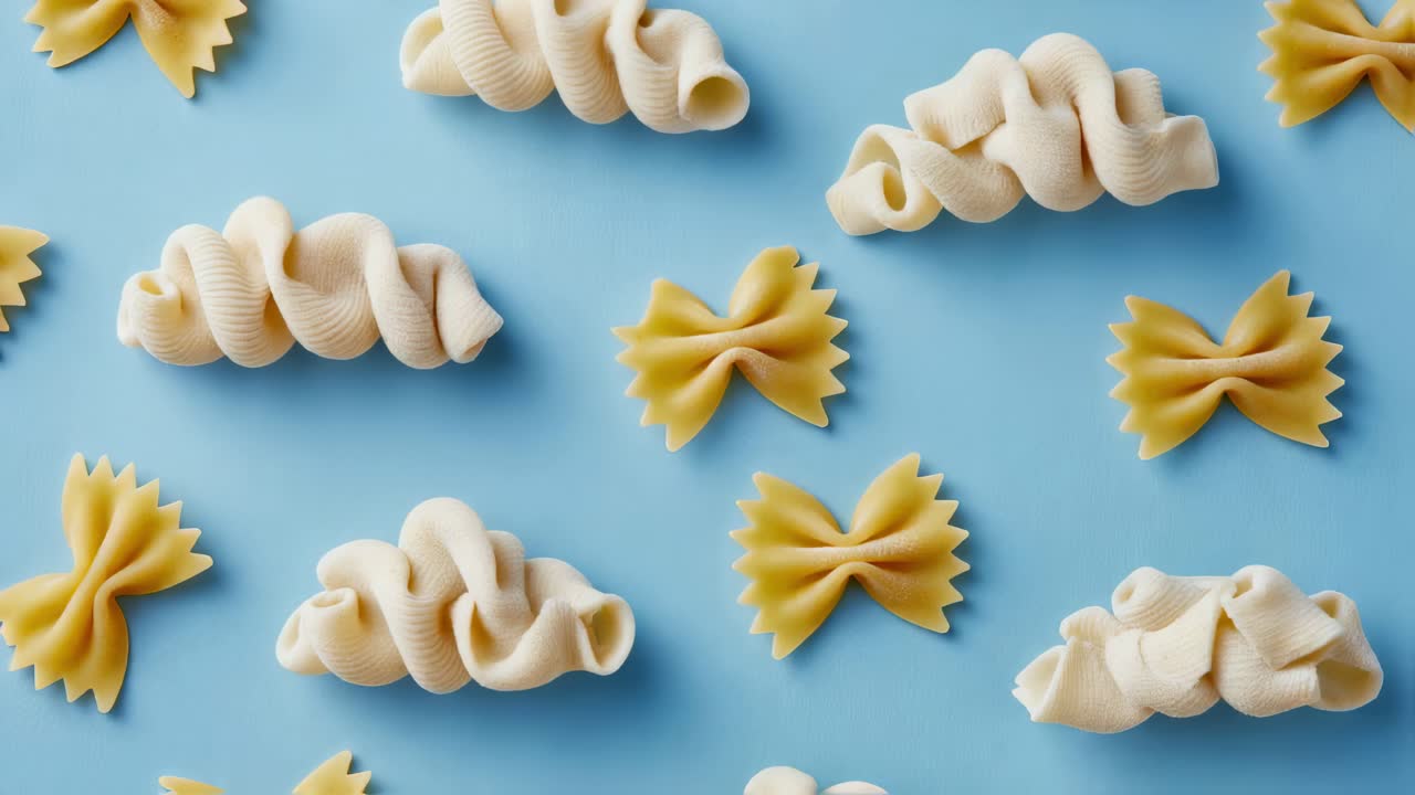 Different pasta shapes, including creste di gallo and farfalle, are arranged on a vibrant blue background, creating a visually appealing pattern with their contrasting colors and textures