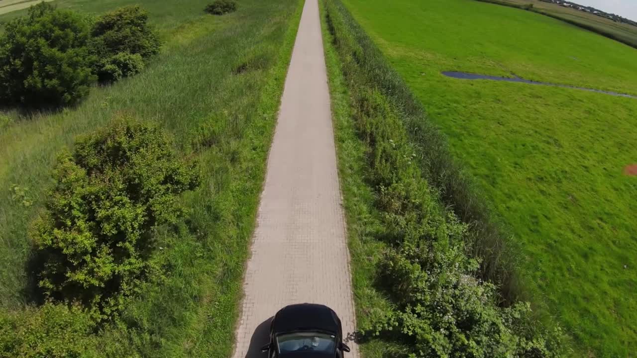 drone shot of a black car driving between fields on a small path