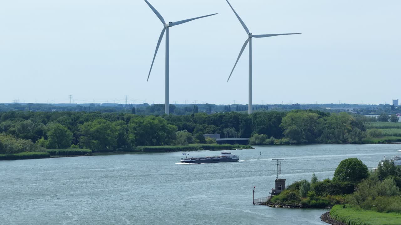 Wind turbines spin by river with passing cargo ship, tranquil scene in Barendrecht