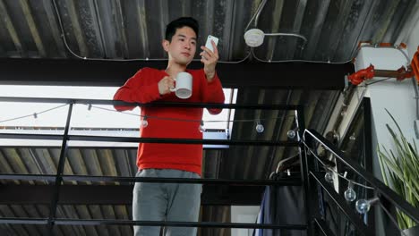 Man-with-coffee-cup-using-mobile-phone-on-railing-4k
