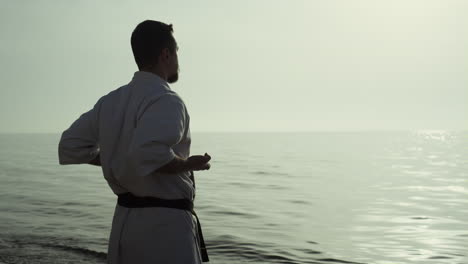 athletic man honing karate technique enjoying sunset on beach back view