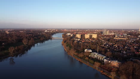 Slow-aerial-backwards-view-of-scenic-blue-lake-surrounded-by-houses-and-autumn-trees-during-dusk