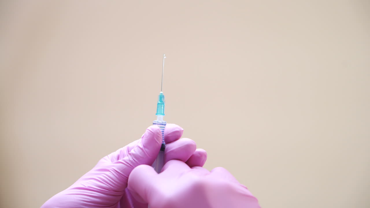Close-up view on a cosmetologists hands in gloves holding syringe with needle for rejuvenating facial injections.