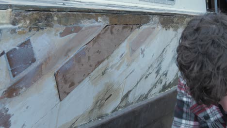 a young man applying epoxy filler to a wooden boat hull repair