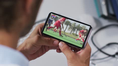 compuesto de un médico masculino viendo un partido de hockey en un teléfono inteligente