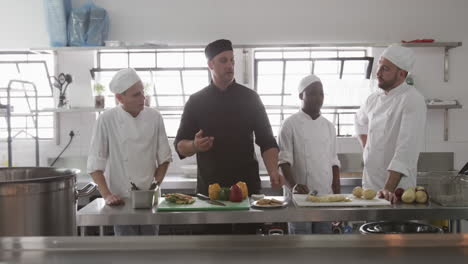 diverse male chef instructing group of trainee male chefs in kitchen, slow motion