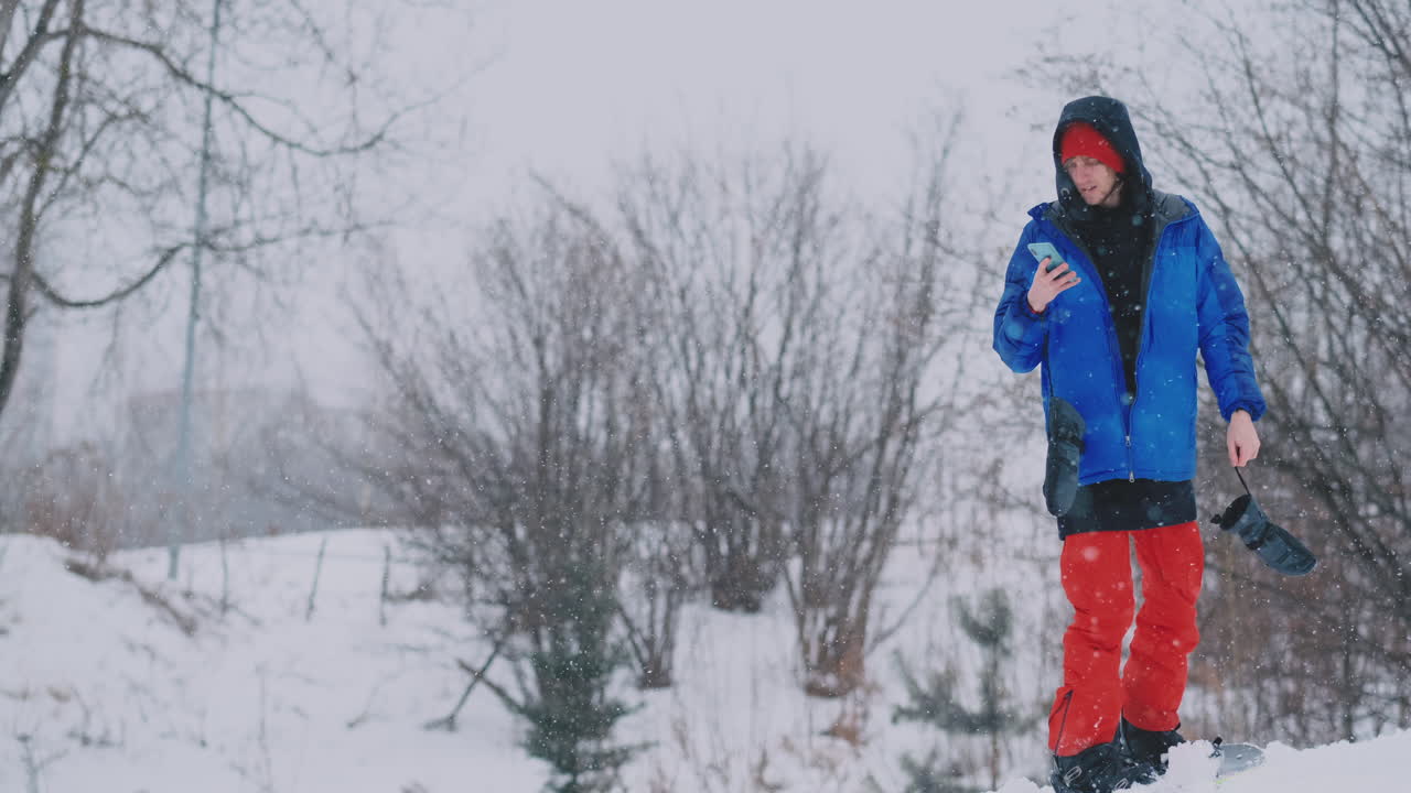 Male snowboarder rides the Board at the ski to the snow slope and writing messages to smartphone to your friends