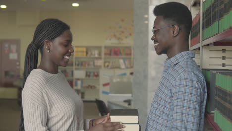 black woman gives some books to a black boy in the library